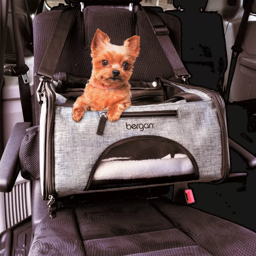 Bergan Booster Soft Pet Carrier is being used in the car. The strap is over the headrest of the car seat. A small dog is sitting inside the carrier, with their head and front legs popped out the top of the carrier.