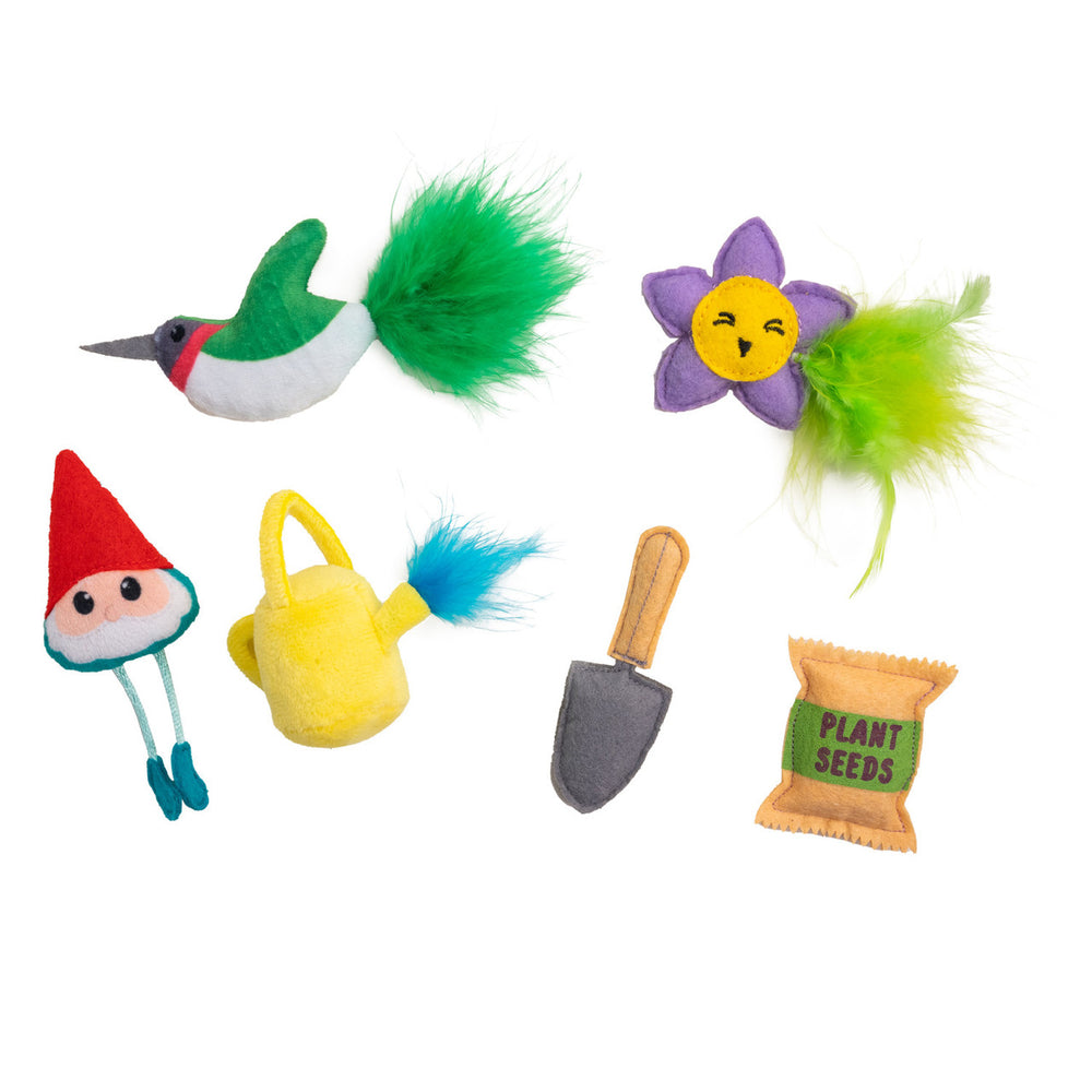 Six colorful garden-themed cat toys arranged on a white background: a green and white hummingbird with a fluffy tail, a purple flower with a smiling yellow face and green feathers, a red-capped garden gnome, a yellow watering can with a blue feather, a gray hand trowel, and a seed packet labeled 'Plant Seeds.'