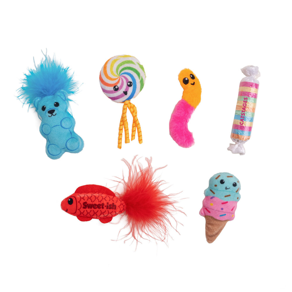 Six candy and dessert-themed cat toys arranged on a white background: a blue gummy bear with a fluffy blue tuft, a rainbow lollipop with yellow strings, a fuzzy pink and orange gummy worm, a pastel-wrapped candy labeled 'Catstages,' a red fish toy labeled 'Sweet-ish' with a red feather tail, and a smiling ice cream cone with blue and pink scoops and sprinkles.
