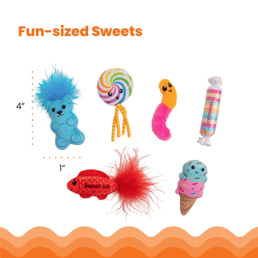 Six candy-themed cat toys displayed on a white background with dimensions marked at approximately 4 inches tall by 1 inch wide. Toys include a blue gummy bear with a fluffy top, a rainbow lollipop with ribbons, a pink and orange gummy worm, a striped wrapped candy labeled 'Catstages,' a red fish with a feather tail labeled 'Sweet-ish,' and a smiling ice cream cone. Fun-sized Sweets.