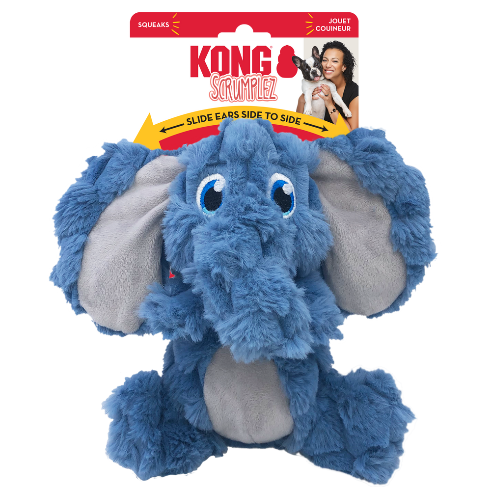 A KONG Scrumplez elephant plush dog toy in its original packaging. The toy is a soft, blue elephant with floppy, oversized ears that have a light gray inner lining. It has embroidered blue eyes and a crinkled texture. The packaging is red and white, displaying the KONG logo, the word 'Scrumplez' in a playful red font. A yellow arrow on the packaging indicates that the toy’s ears slide from side to side. The packaging also highlights that the toy squeaks.
