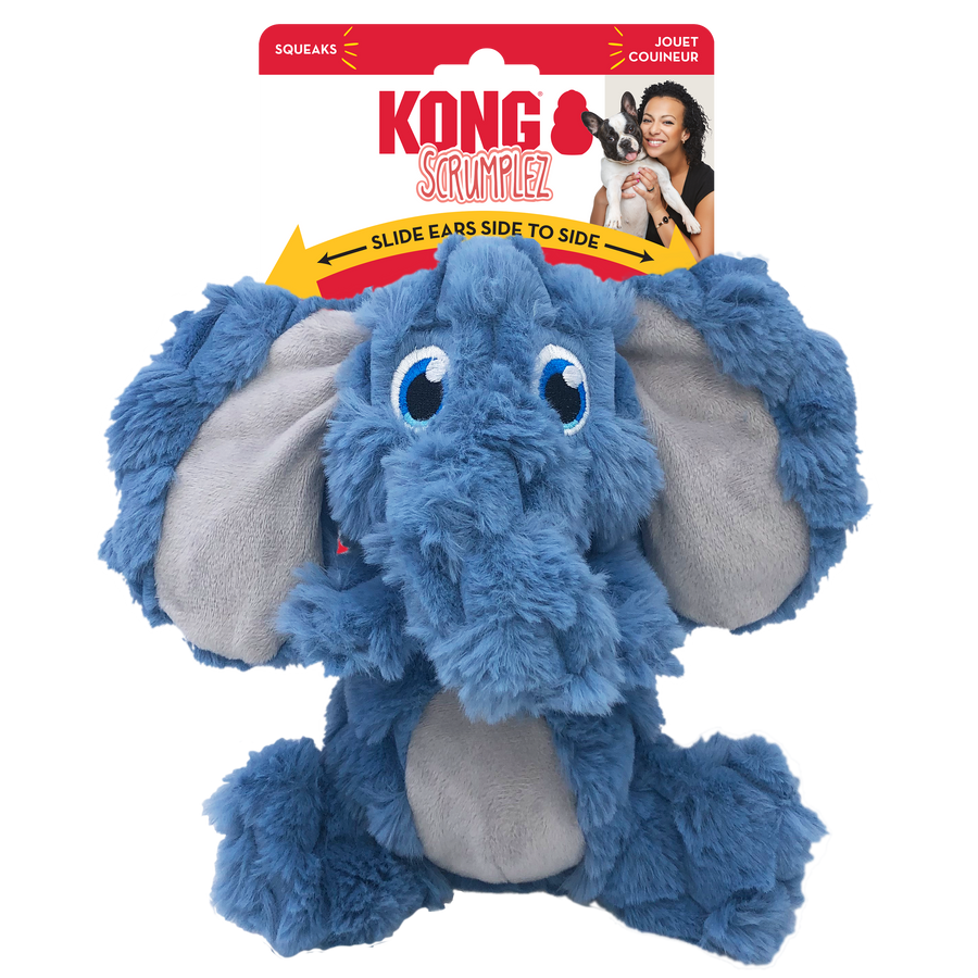 A KONG Scrumplez elephant plush dog toy in its original packaging. The toy is a soft, blue elephant with floppy, oversized ears that have a light gray inner lining. It has embroidered blue eyes and a crinkled texture. The packaging is red and white, displaying the KONG logo, the word 'Scrumplez' in a playful red font. A yellow arrow on the packaging indicates that the toy’s ears slide from side to side. The packaging also highlights that the toy squeaks.