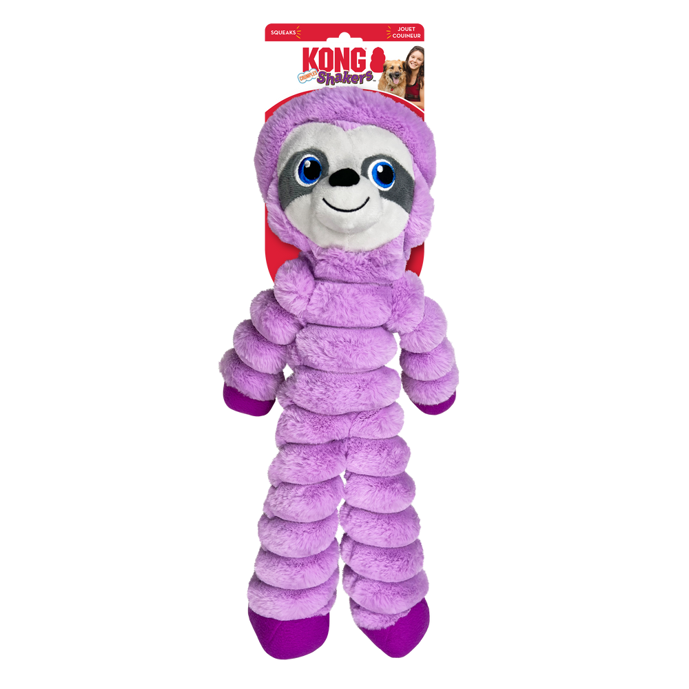 A KONG Shakers Crumples sloth plush dog toy in its original packaging. The toy is soft and purple with a smiling sloth face featuring embroidered blue eyes, a black nose, and gray facial markings. Its body is segmented with a crinkled texture, and the arms and legs are long and floppy with darker purple feet. The packaging is red and white, displaying the KONG logo, the word 'Shakers' in a playful pink and red font. The packaging also highlights that the toy squeaks.