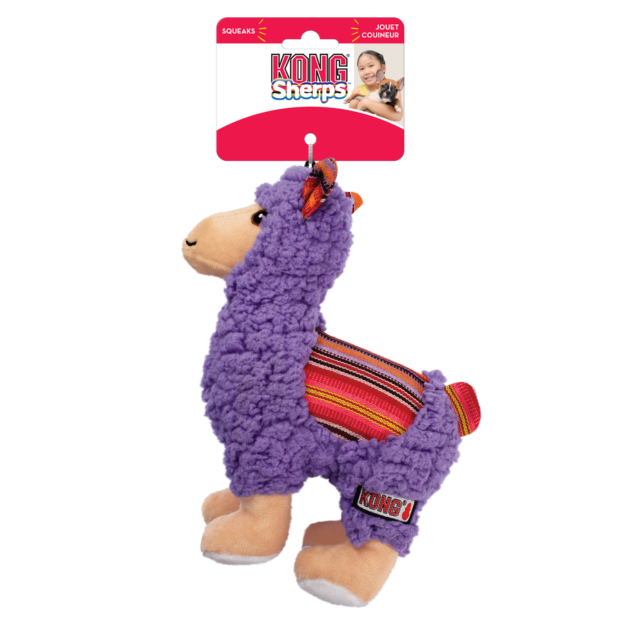 A KONG Sherps llama plush dog toy in its original packaging. The toy has a soft, purple fleece-like body with a beige muzzle and embroidered eyes. Its ears feature a colorful woven fabric with red, orange, and yellow stripes, which matches the saddle-like fabric on its back. The llama stands on beige plush legs with white hooves, and it has a small, fluffy tail. The packaging is red and white, displaying the KONG logo, the word 'Sherps' in a playful blue font, also highlights that the toy squeaks.