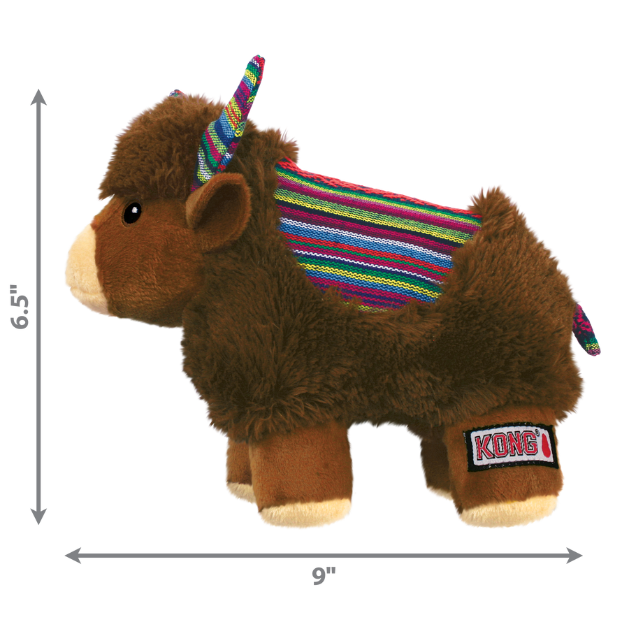 A KONG Sherps yak plush dog toy, measuring approximately 6.5 inches in height and 9 inches in width. The toy has a soft, brown furry body with a beige muzzle and embroidered eyes. Its ears and curved horns feature a colorful woven fabric with bright striped patterns, which match the saddle-like fabric on its back. The yak stands on beige plush legs with white hooves and has a short, fluffy tail. Measurement arrows along the sides indicate the toy’s dimensions.