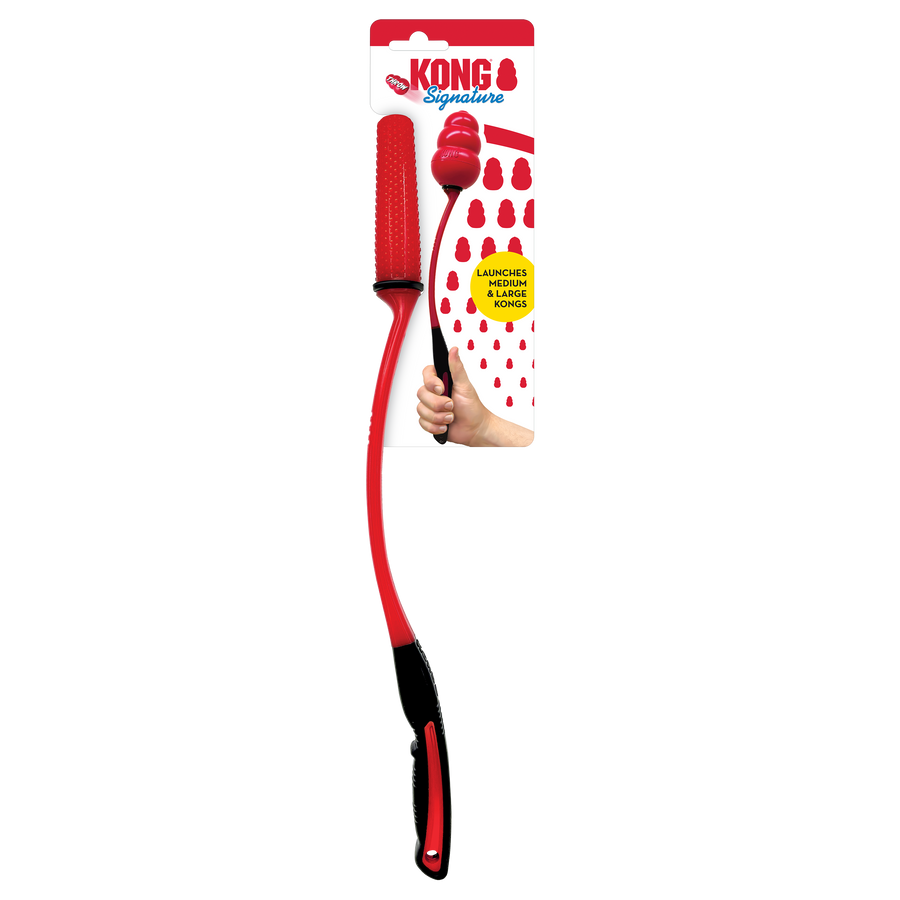 A KONG Signature KONG Throw toy in its original packaging. The toy consists of a long, flexible red and black throwing stick with a textured red handle for grip. At the end, it holds a classic red KONG-shaped rubber toy designed for fetching. The packaging is red and white, displaying the KONG logo with the word 'Signature' in blue. A yellow label highlights that the thrower is designed to launch medium and large KONG toys. There is also an image of a hand gripping the thrower to demonstrate its use.