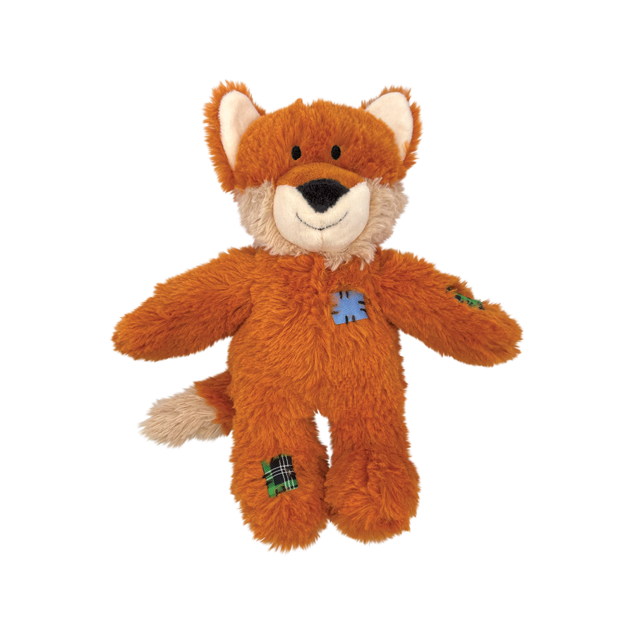 A plush fox dog toy from KONG Wild Knots, featuring a soft orange fur exterior with a white muzzle and inner ears. The toy has a friendly, smiling expression and includes stitched patch details on its body and limbs for a rustic look. It is designed with an internal knotted rope structure for durability, while the plush exterior provides comfort for dogs during play and snuggles.