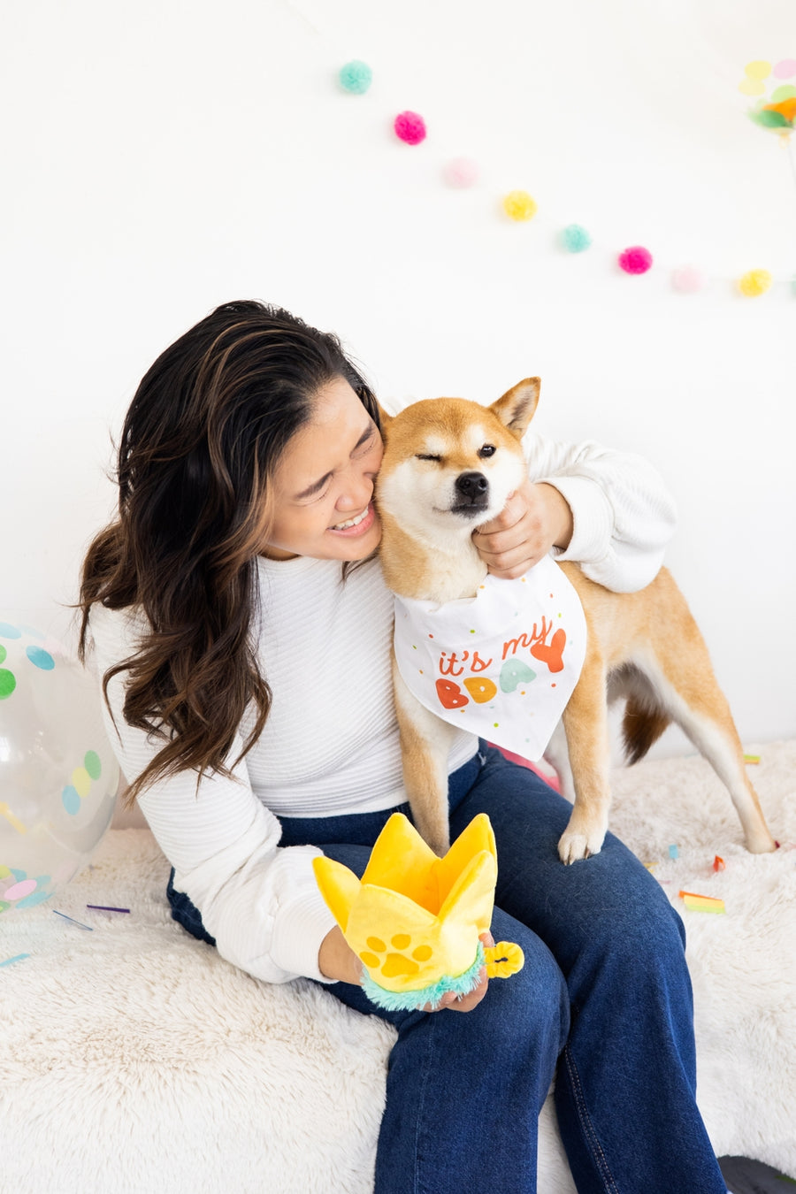 Pearhead Happy Barkday Medium/Large Bandana and Hat Set, a woman hugging a Shiba Inu dog wearing the white "It's My B'Day" bandana, with the yellow crown hat toy
