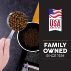 Hand holding a measuring cup filled with pet food, with 'Made in our USA Kitchens' and 'Family Owned Since 1926' text on a dark background.