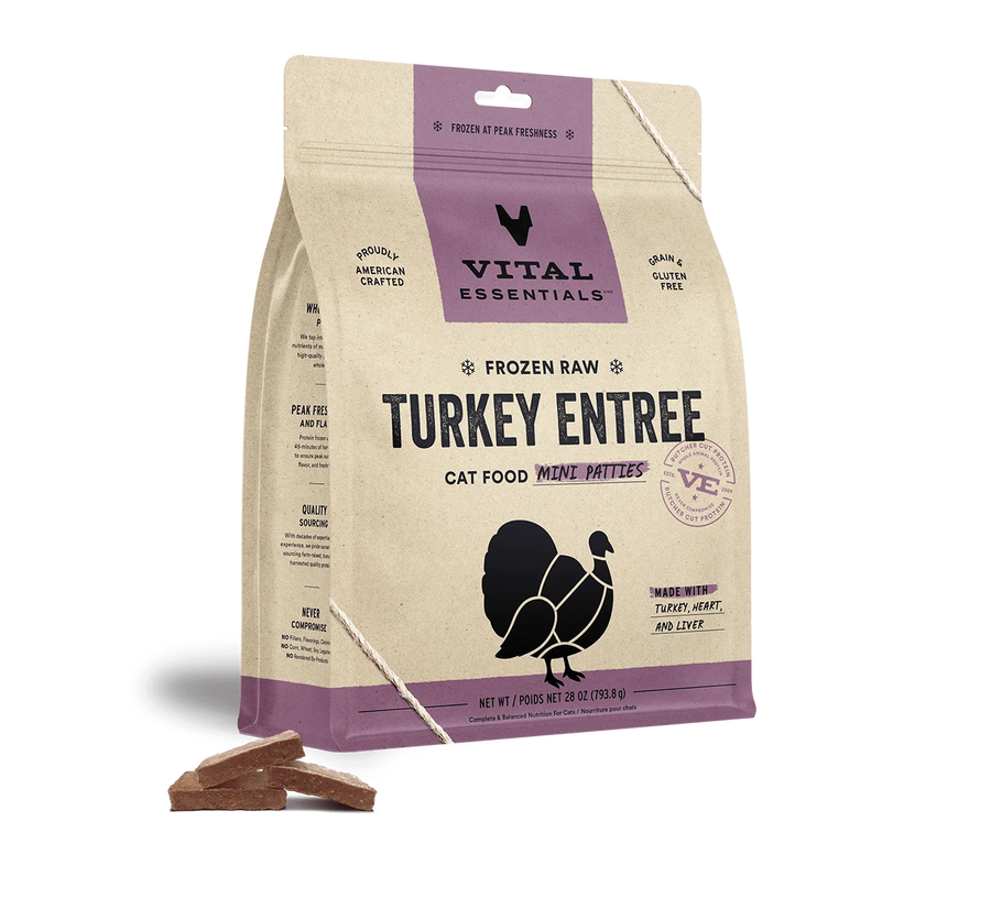A beige and purple bag of Vital Essentials Frozen Raw Turkey Entree Mini Patties for cats. The bag features the Vital Essentials logo and the text 'Frozen Raw Turkey Entree Cat Food Mini Patties.' The packaging highlights benefits like grain and gluten-free, proudly American crafted, and made with turkey, heart, and liver. A silhouette of a turkey is displayed on the front. A few of the brown mini patties are scattered at the base of the bag, showing their square shape and food texture.