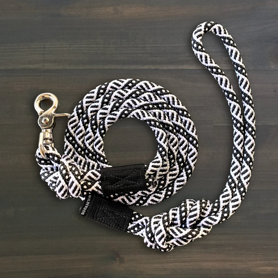 Wilderdog Quick Clip Dog Rope Leash in black and white geometric pattern coiled on a wooden surface, showing the braided rope, silver swivel clip, and knotted handle with Wilderdog label.