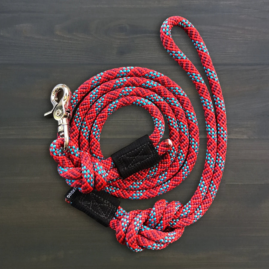 Wilderdog Quick Clip Dog Rope Leash coiled on dark wood surface, red and teal braided rope with silver snap clip and black Wilderdog branded grip.
