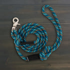 Wilderdog Quick Clip Dog Rope Leash in Pacific Blue coiled on dark wood surface, teal braided rope with multicolor speckle pattern, silver snap clip, and black Wilderdog branded grip.
