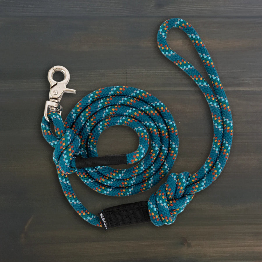 Wilderdog Quick Clip Dog Rope Leash in Pacific Blue coiled on dark wood surface, teal braided rope with multicolor speckle pattern, silver snap clip, and black Wilderdog branded grip.