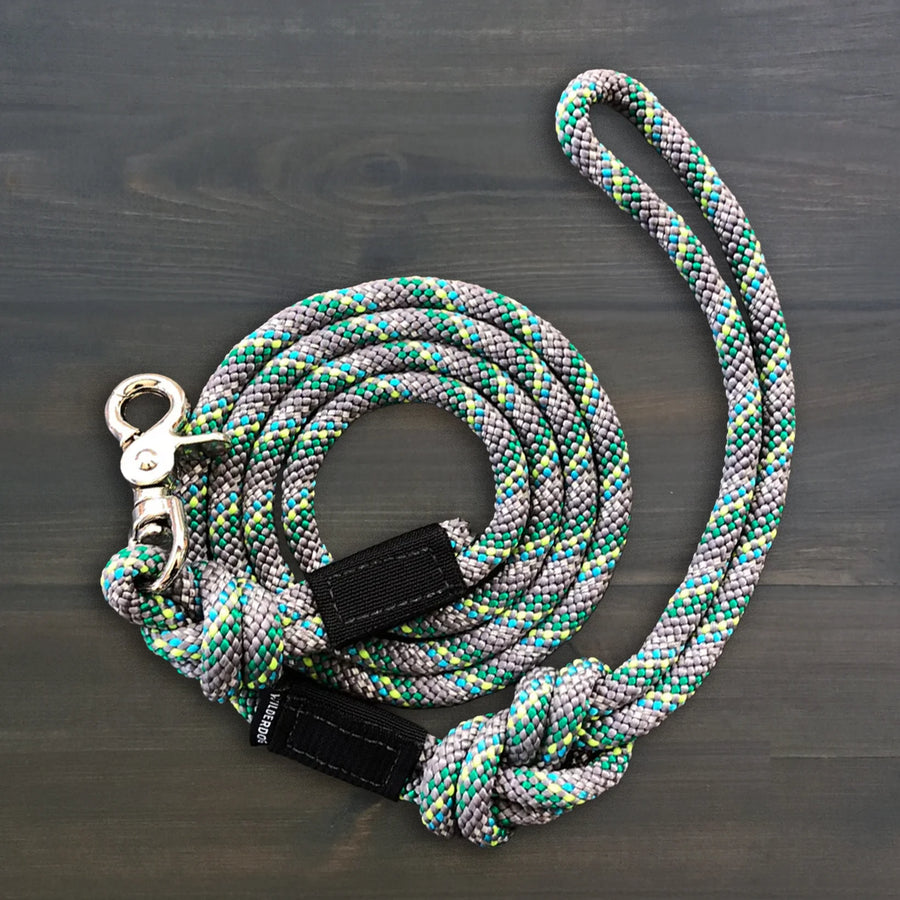 Wilderdog Quick Clip Reflective Dog Rope Leash in Alpine colorway coiled on dark wood surface, gray, teal, and yellow-green braided rope with silver snap clip and black Wilderdog branded grip.