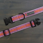Wilderdog Lilac ultralight dog collar laid flat on dark wood surface, showing light pink webbing with orange and teal geometric woven pattern, Wilderdog logo patch, black D-ring, and quick-release buckle.