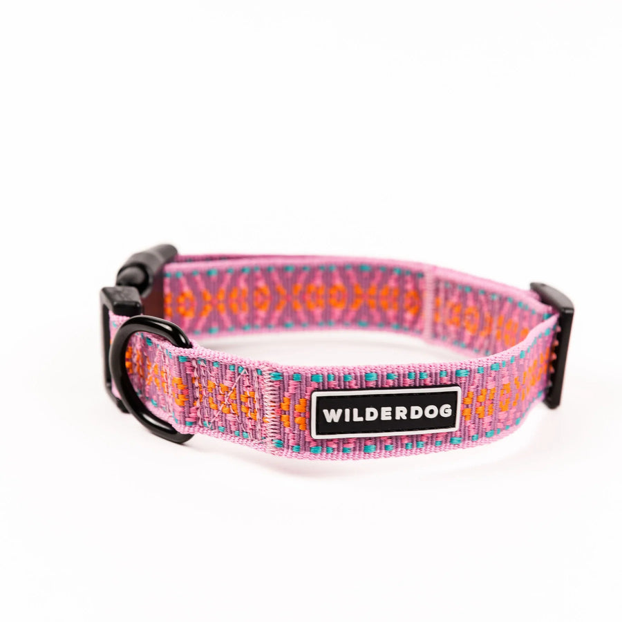 Wilderdog Lilac ultralight dog collar looped upright on white background, showing light pink webbing with orange diamond and teal dot geometric woven pattern, black D-ring, quick-release buckle, and Wilderdog logo patch.