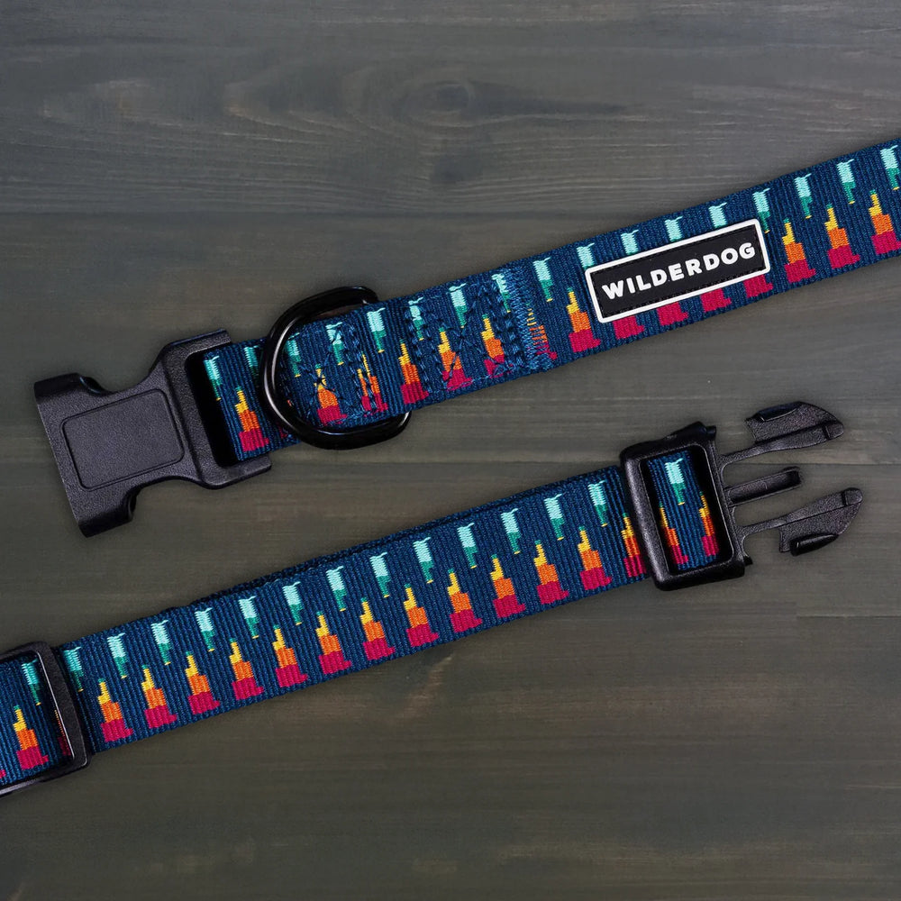 Wilderdog Marina ultralight dog collar laid flat on dark wood surface, showing navy webbing with multicolor flame-and-teal geometric pattern, Wilderdog logo patch, black D-ring, and quick-release buckle.
