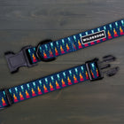 Wilderdog Marina ultralight dog collar laid flat on dark wood surface, showing navy webbing with multicolor flame-and-teal geometric pattern, Wilderdog logo patch, black D-ring, and quick-release buckle.