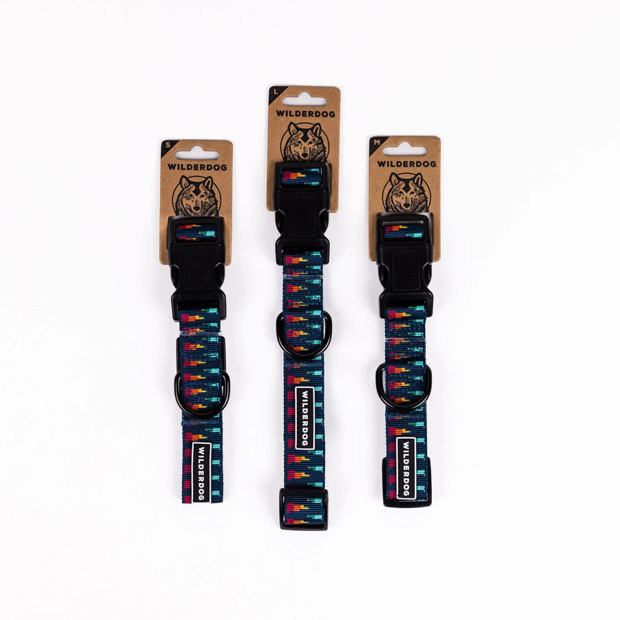 Three Wilderdog Marina ultralight dog collars in Small, Medium, and Large sizes displayed on branded kraft paper hang tags against a white background, showing navy webbing with multicolor geometric pattern.