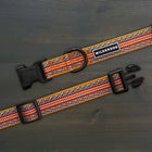 Wilderdog Sienna ultralight dog collar laid flat on dark wood surface, showing amber orange webbing with red, teal, and white chevron zigzag woven pattern, Wilderdog logo patch, black D-ring, and quick-release buckle.