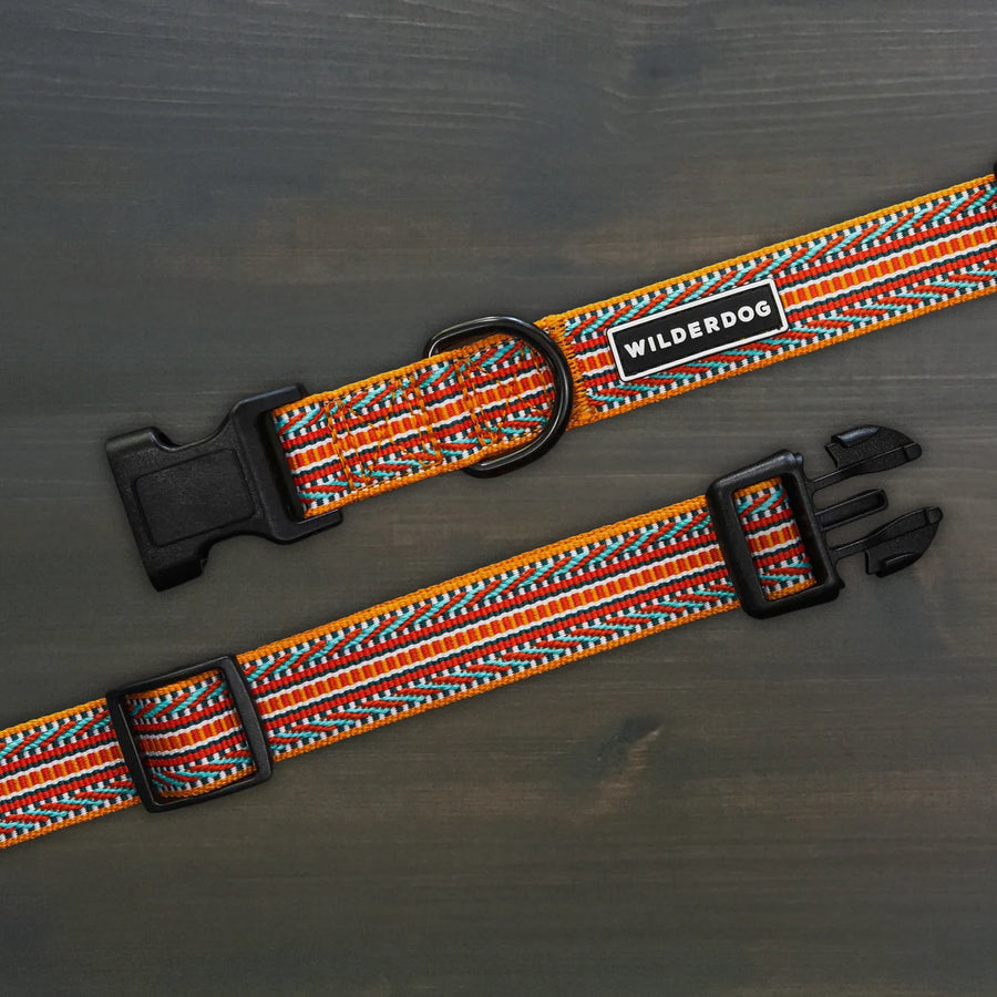 Wilderdog Sienna ultralight dog collar laid flat on dark wood surface, showing amber orange webbing with red, teal, and white chevron zigzag woven pattern, Wilderdog logo patch, black D-ring, and quick-release buckle.