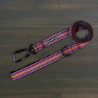 Wilderdog Ultralight Dog Leash in Daybreak laid flat on dark wood surface, pink, orange, teal, and yellow chevron woven pattern with black Wilderdog carabiner clip, D-ring, and branded label.