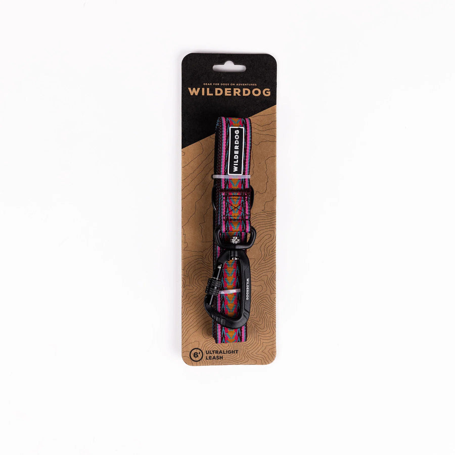 Wilderdog Ultralight Dog Leash in Daybreak displayed in retail packaging on a kraft paper card with topographic map design, showing the 6-foot leash with pink, orange, and teal chevron pattern and black carabiner clip.