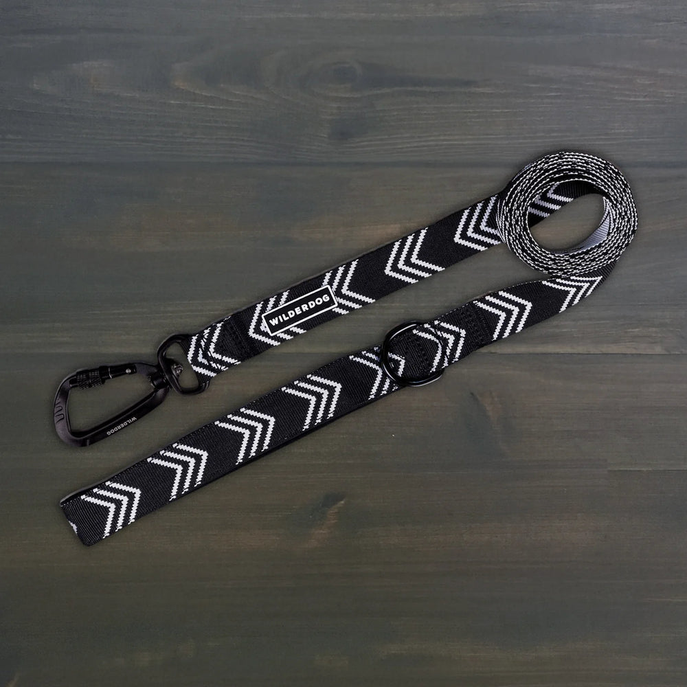 Wilderdog Ultralight Dog Leash in black and white chevron pattern laid flat on dark wood surface, showing black Wilderdog carabiner clip, D-ring, and branded label.
