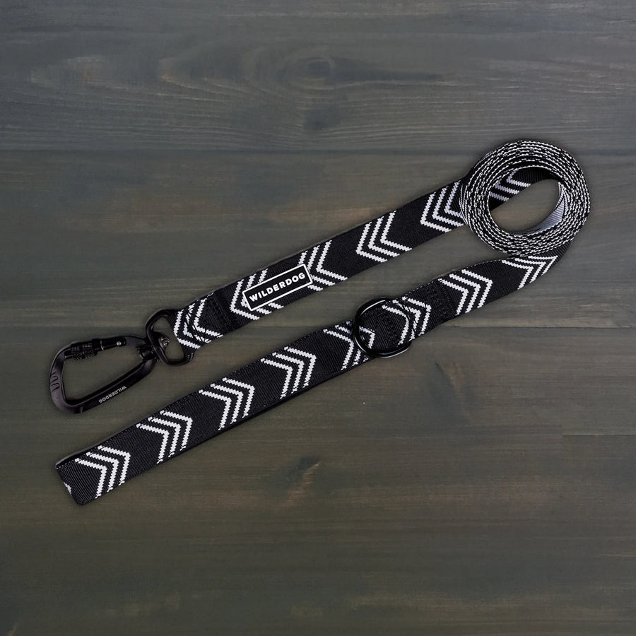 Wilderdog Ultralight Dog Leash in black and white chevron pattern laid flat on dark wood surface, showing black Wilderdog carabiner clip, D-ring, and branded label.