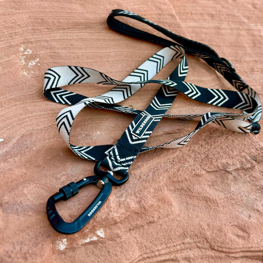 Close-up of Wilderdog Ultralight Dog Leash in black and white chevron pattern draped on red sandstone, showing black Wilderdog carabiner clip and Wilderdog branded label.