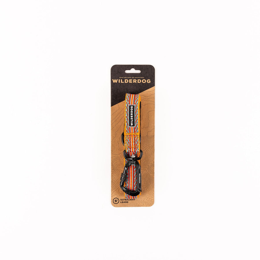 Wilderdog Ultralight Dog Leash in Sienna displayed in retail packaging on a kraft paper card with topographic map design, showing the 6-foot leash with orange, red, and teal striped pattern and black carabiner clip.