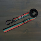 Wilderdog Ultralight Dog Leash in Trout pattern laid flat on dark wood surface, red, teal, and orange gradient woven webbing with black Wilderdog carabiner clip, D-ring, and branded label.