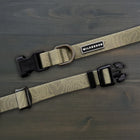Wilderdog Olive waterproof dog collar laid flat on dark wood surface, showing olive green coated webbing with subtle topo map line pattern, Wilderdog logo patch, brass-tone D-ring, and black quick-release buckle.